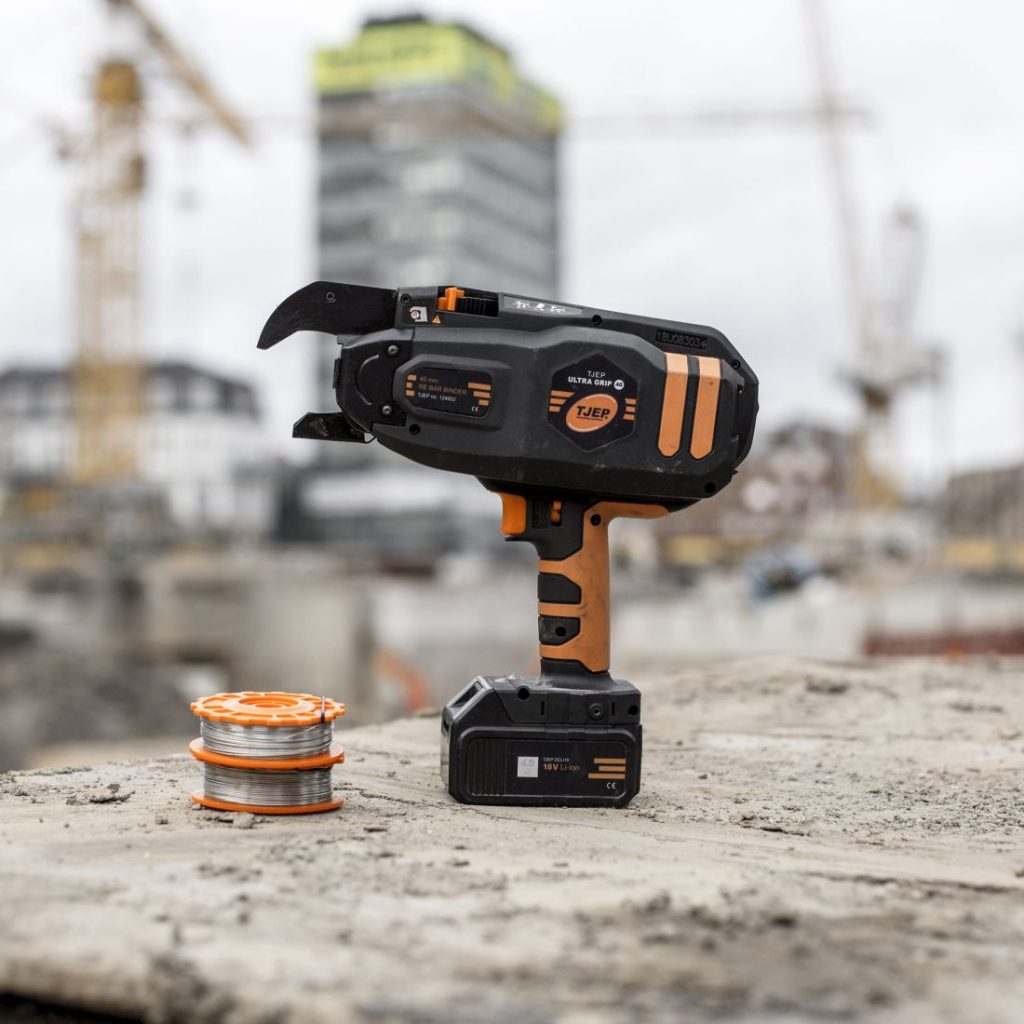 Tjep Sidoskone ULTRA GRIP 40 12-40 mm 4,0Ah Li-ion sivulta työmaalla. Kuvassa myös kaksi sidoslankarullaa.