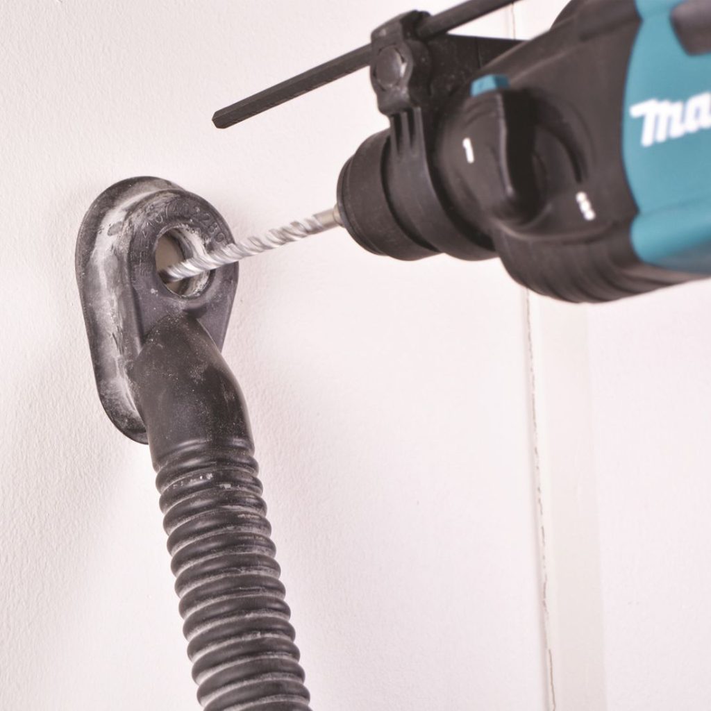 MAKITA Pölynimulisälaite. Lähikuvassa pölynimulisälaite kiinnitettynä seinään työmiehen poratessa seinään reikää.
