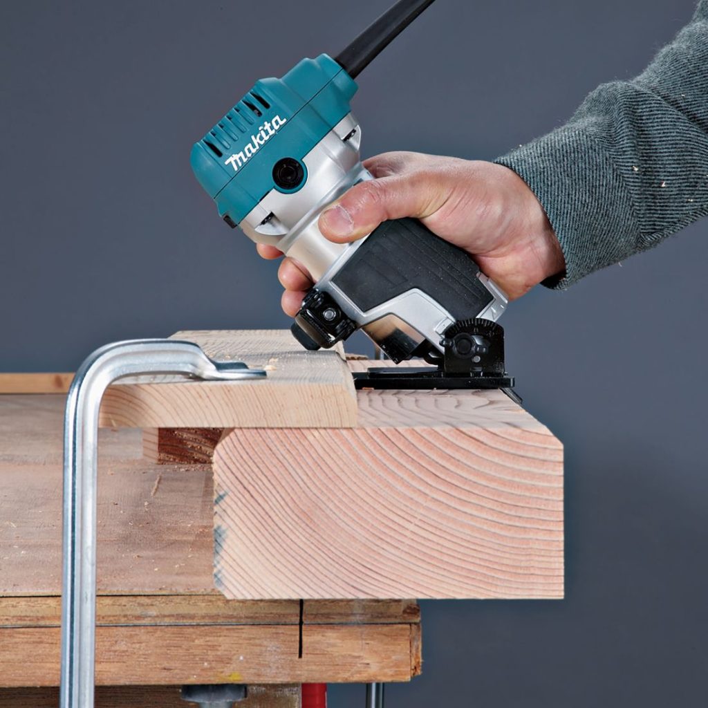 MAKITA Kulmaohjain RT0700C, RT0702C, DRT50. Kuvassa henkilö jyrsimässä palkin reunaa kulmaohjainta hyväksikäyttäen.
