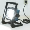 MAKITA LED-valaisin LXT. Kuvassa LED-valaisin LXT oikealta etuyläviistosta valaisin päällä ja yhdistettynä seinäpistokkeeseen virtajohdon avulla.