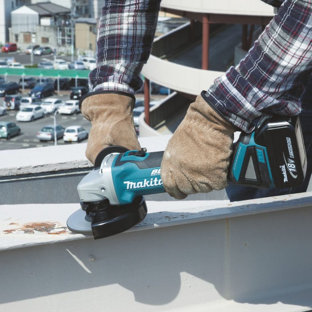MAKITA Kulmahiomakone LXT. Kuvassa henkilö hiomasssa teräs I-palkkia kulmahiomakone LXT:n avulla.