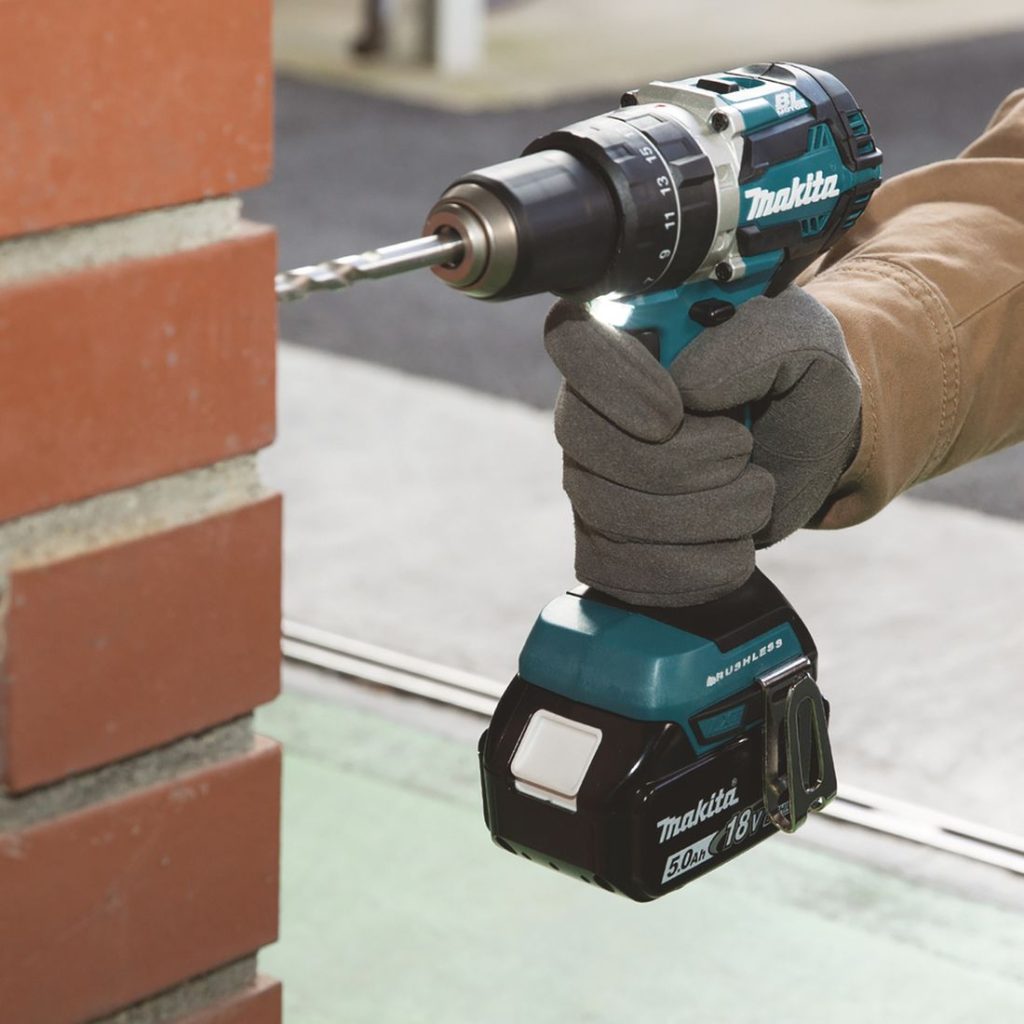 MAKITA Iskuporakone LXT. Kuvassa henkilö poraamassa reikää tiiliseinään iskuporakoneen avulla.