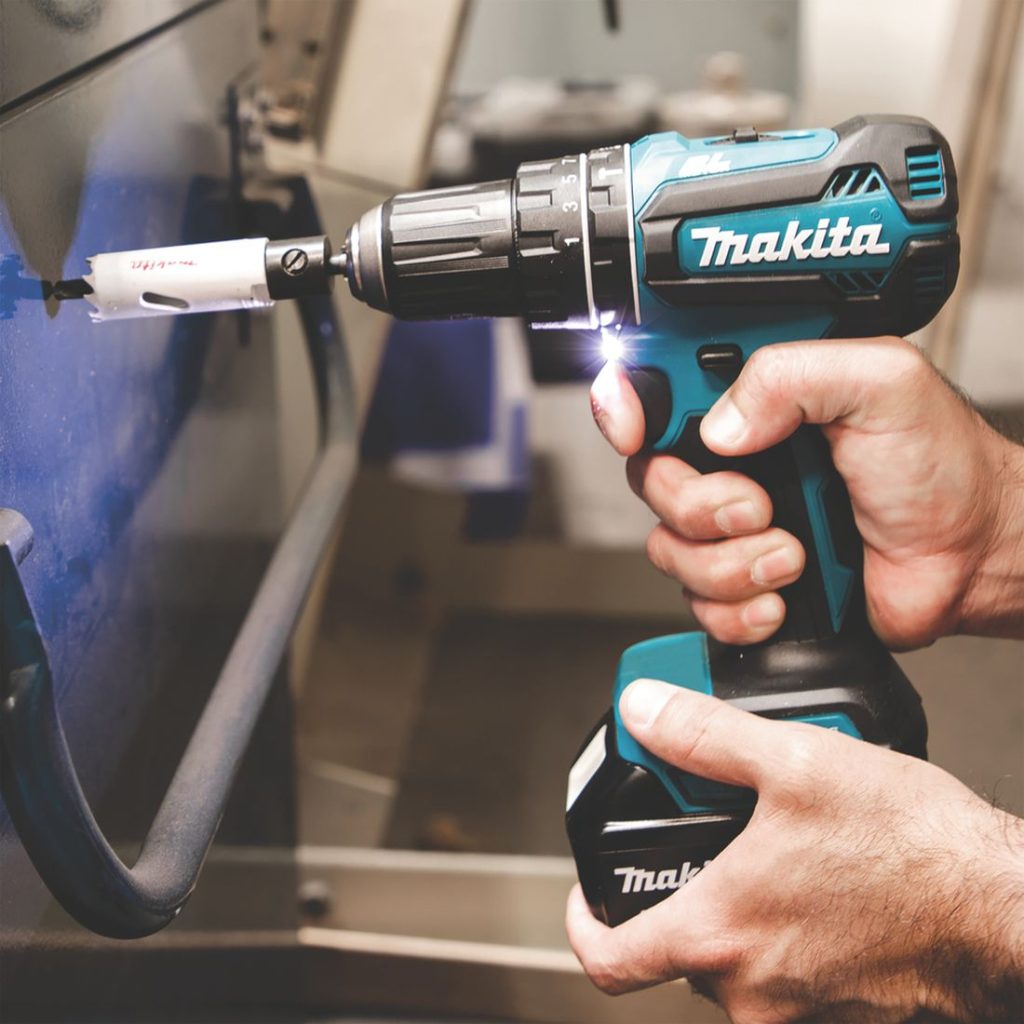 MAKITA Iskuporakone LXT. Kuvassa henkilö poraamassa reikää kaakeloituun seinään iskuporakoneen avulla.