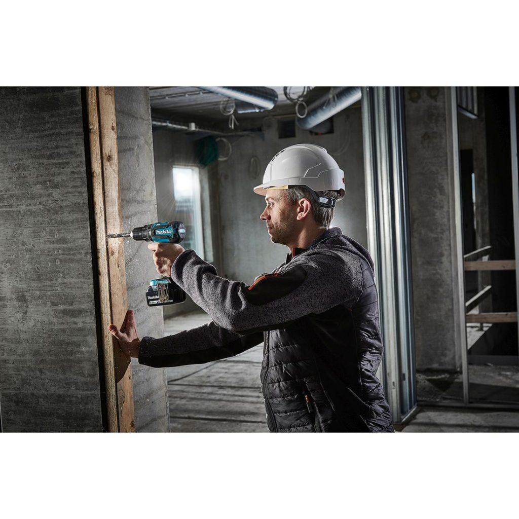 MAKITA Iskuporakone LXT. Kuvassa henkilö poraamassa reikää laudan läpi betoniseinään iskuporakoneen avulla.