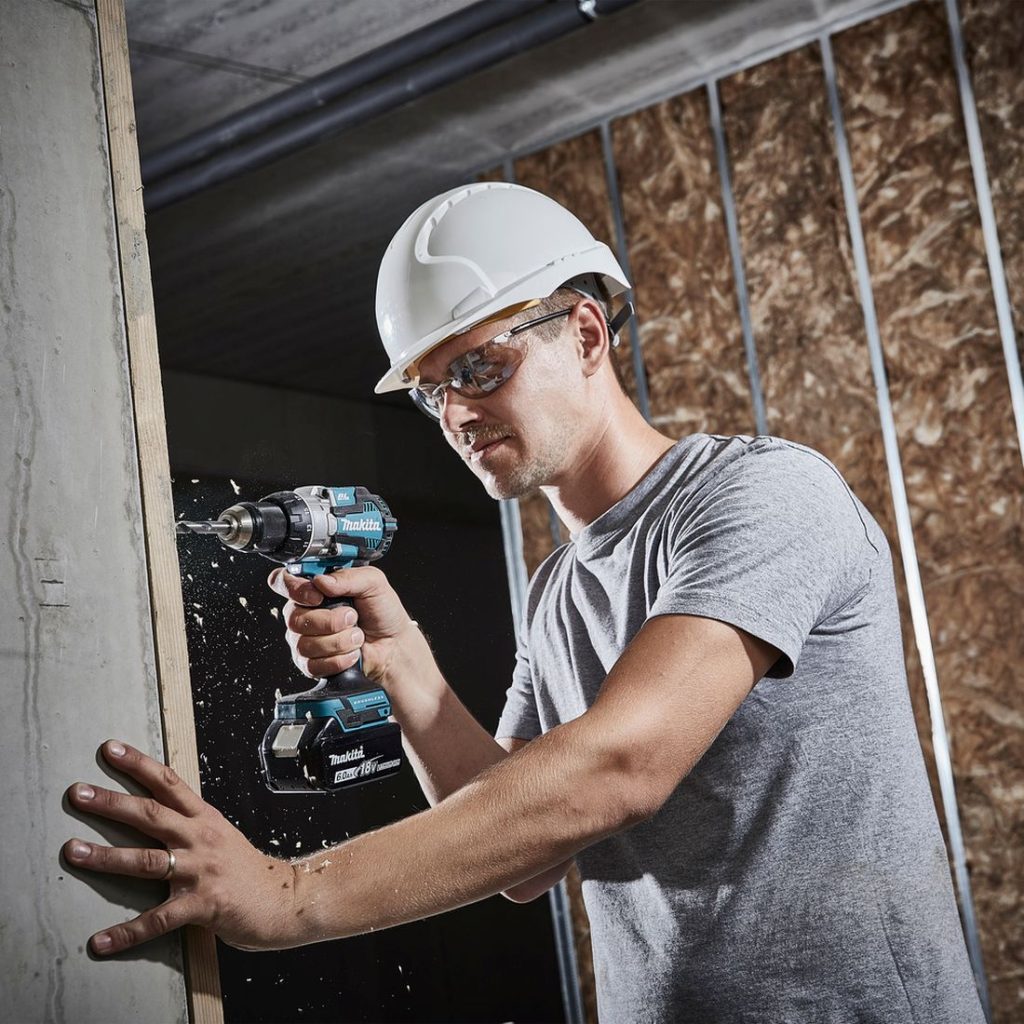 MAKITA Iskuporakone LXT. Kuvassa henkilö poraamassa laudan läpi betoniin iskiporakone LXT:n avulla.