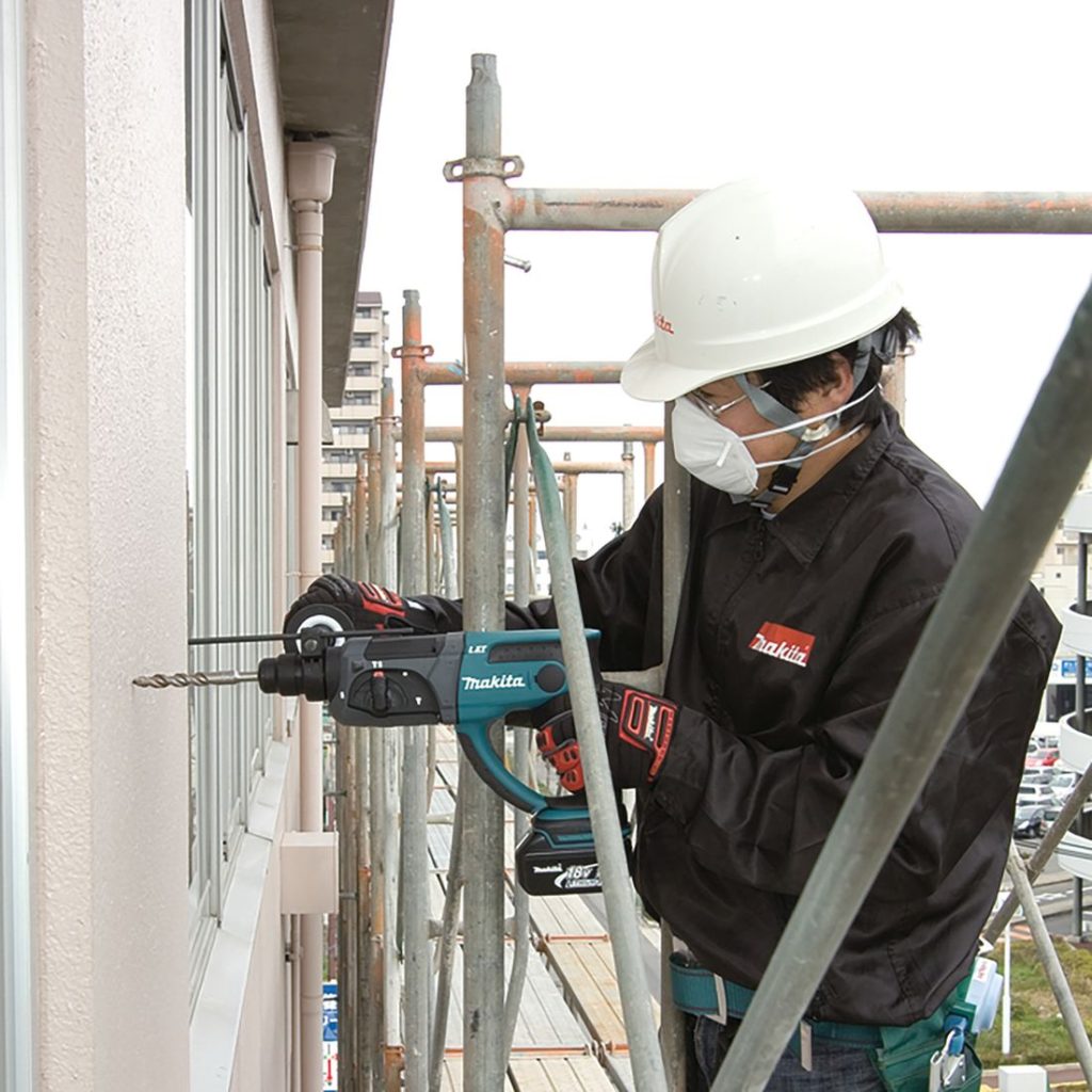 MAKITA Poravasara LXT. Kuvassa henkilö rakennustelineellä poraamassa reikää betoniseinään Poravasara LXT:n avulla.