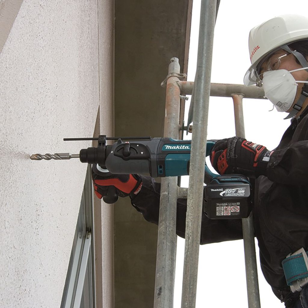 MAKITA Poravasara LXT. Kuvassa henkilö rakennustelineellä poraamassa reikää betoniseinään Poravasara LXT:n avulla.
