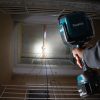 MAKITA LED-valaisin LXT. Kuvassa henkilö valaisemassa kattoon kiinnitettyä siltanosturia pimeässä porraskäytävässä LED-valaisin LXT:n avulla.