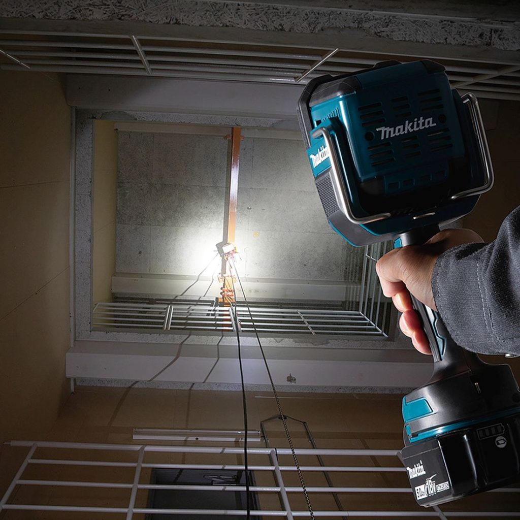 MAKITA LED-valaisin LXT. Kuvassa henkilö valaisemassa kattoon kiinnitettyä siltanosturia pimeässä porraskäytävässä LED-valaisin LXT:n avulla.