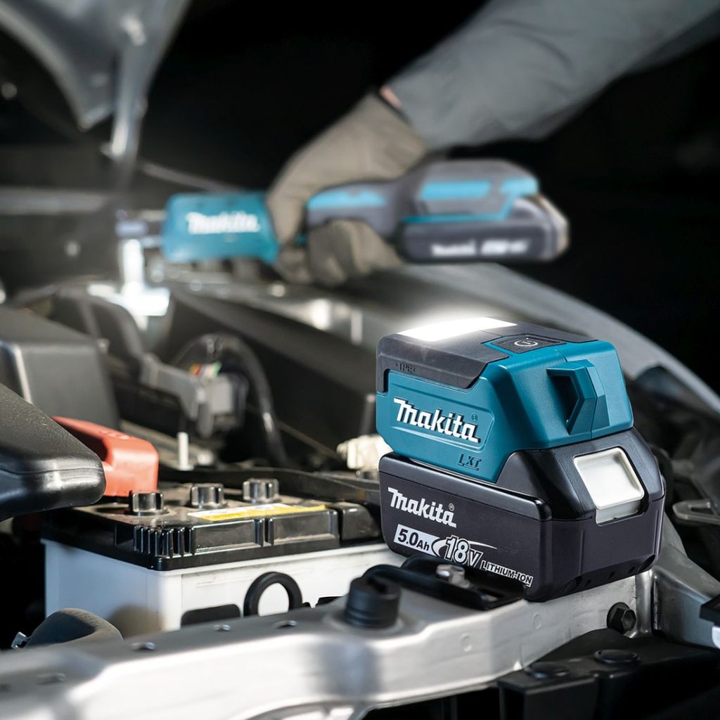 MAKITA LED-valaisin LXT. Kuvassa henkilö korjaamassa autoa LED-valaisin LXT:n avulla . Kuva valaisimesta vasemmalta takayläviistosta.