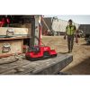 Milwaukee M18 FORGE DBSC 2-paikkainen pikalaturi. Kuvassa pikalaturi auton perälaudalla vasemmalta etuviistosta. Henkilö taustalla kantaa Milwaukee konetta ja akkua käsissään.