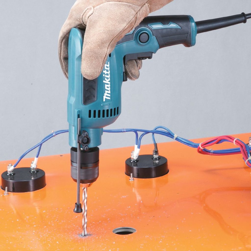 MAKITA Porakone DP2011. Kuvassa henkilö poraamassa metallisen ohjauspaneelin takapuolelle reikää Porakone DP2011:n avulla.