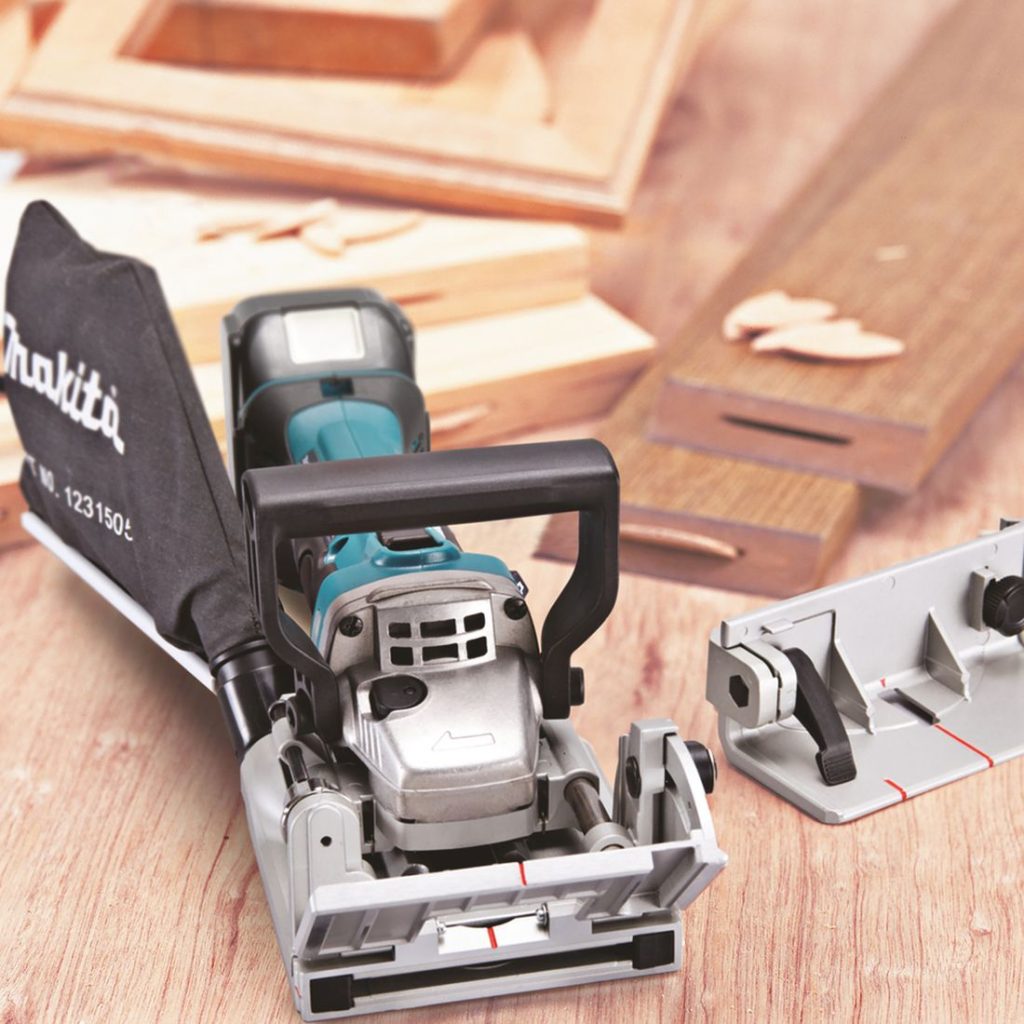 MAKITA Liitosjyrsin LXT. Kuvassa Liitosjyrsin LXT työpöydällä vasemmalta etuyläviistosta. Liitosjyrsimellä tehty taulun kehyksiä.