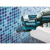 MAKITA Monitoimikone LXT. Kuvassa henkilö irrottamassa kaakelisaumoja kylpyhuoneen kaakeliseinästä Monitoimikone LXT:n avulla.
