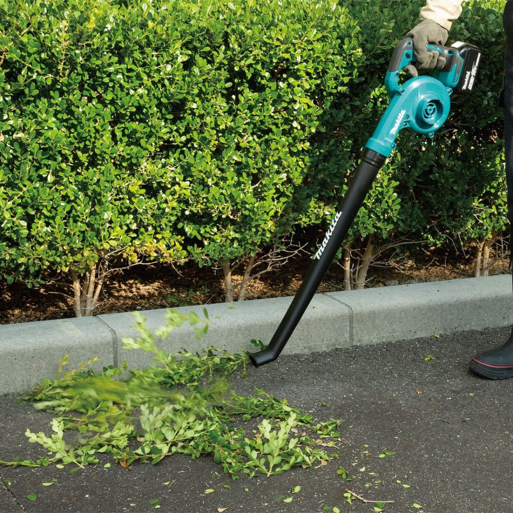 MAKITA Puhallin LXT. Kuvassa henkilö puhaltamassa pensaan lehtiä Puhallin LXT:n avulla.