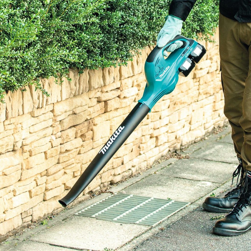 MAKITA Puhallin LXT. Kuvassa henkilö puhaltamassa roskia kivilaatoista Puhallin LXT:n avulla.