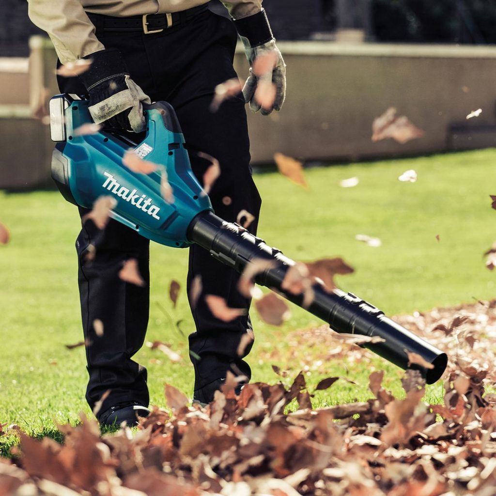 MAKITA Puhallin LXT. Kuvassa henkilö puhaltamassa puun lehtiä nurmikolta Puhallin LXT:n avulla.