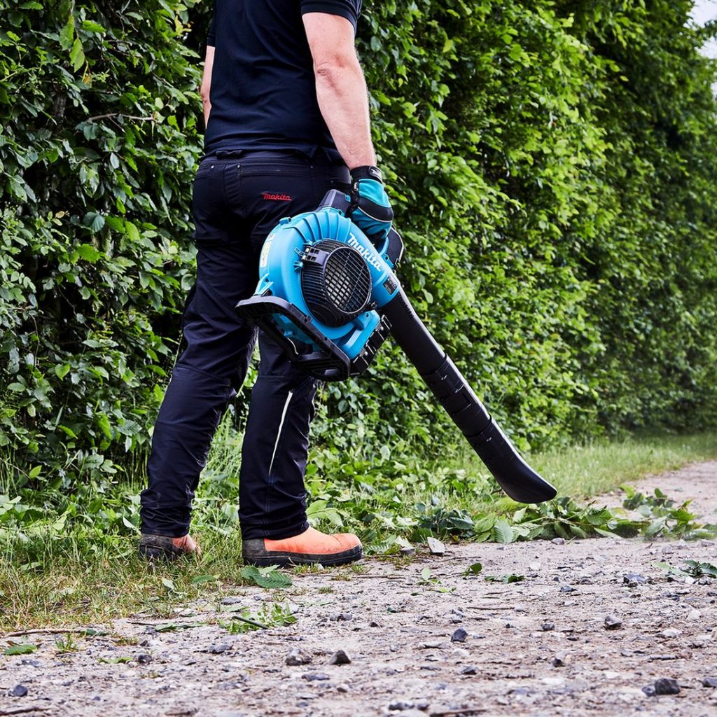 MAKITA Puhallin LXT. Kuvassa henkilö puhaltamassa puun lehtiä kadulla Puhallin LXT:n avulla.