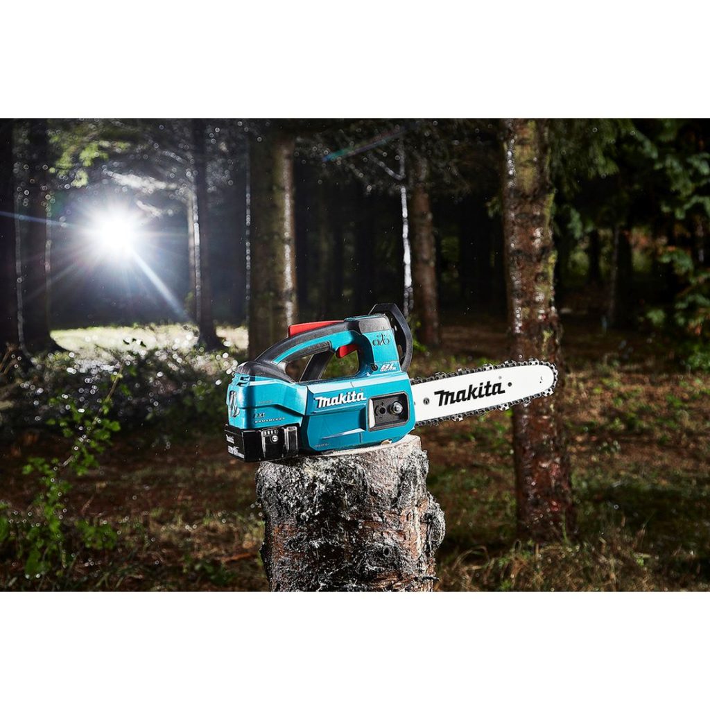 MAKITA Ketjusaha LXT. Kuvassa Ketjusaha LXT kannon päällä pimeässä metsässä. Taustalla loistaa valo.