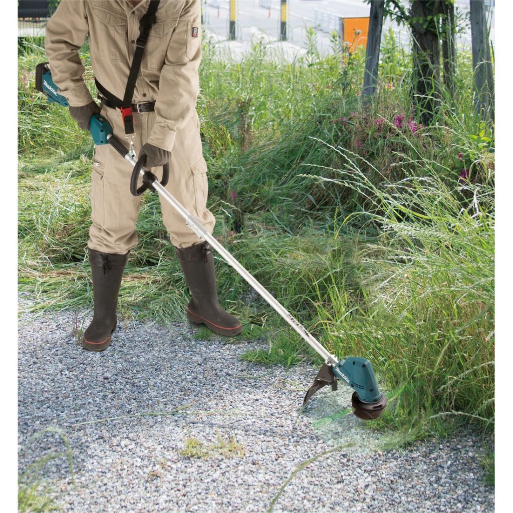 MAKITA Ruohotrimmeri LXT. Kuvassa henkilö trimmaamassa nurmikkoa pensaan ympäriltä Ruohotrimmeri LXT:n avulla.