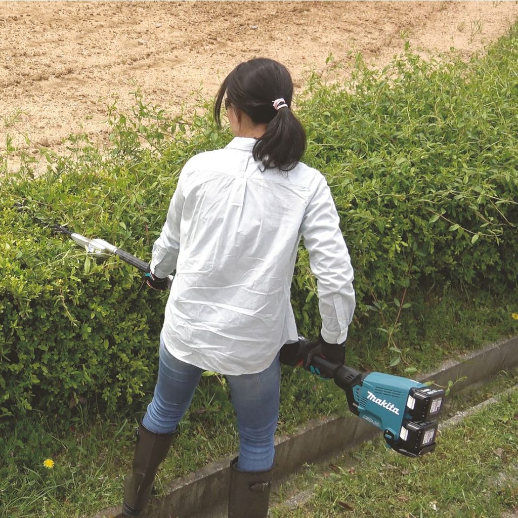 MAKITA Puutarhan monitoimikone LXT. Kuvassa henkilö trimmaamassa matalaa pensasaitaa monitoimikone LXT:n avulla.