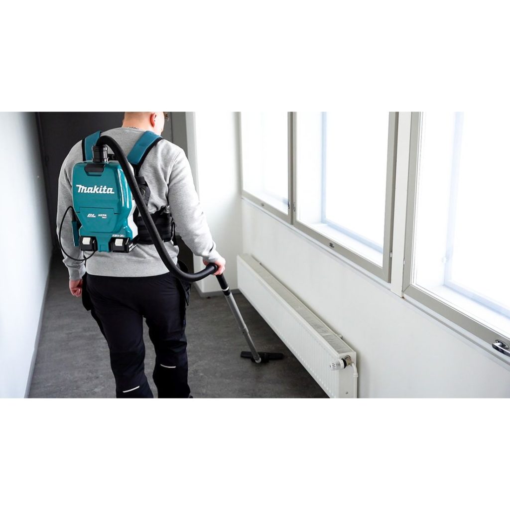 MAKITA Reppuimuri LXT. Kuvassa henkilö kantaa Reppuimuri LXT:tä selässään imuroidessaan käytävää.