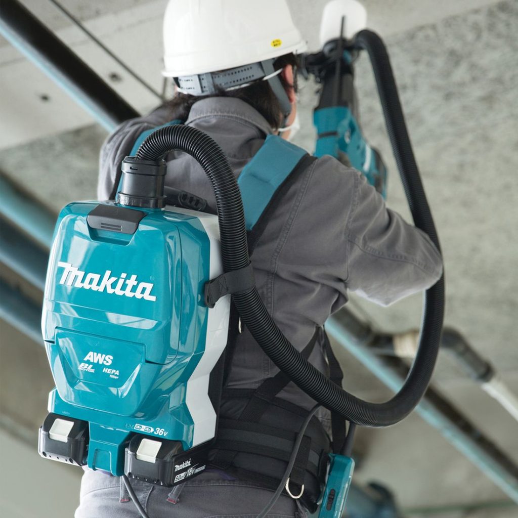 MAKITA Reppuimuri LXT. Kuvassa henkilöllä Reppuimuri LXT selässään poratessaan alapuolelta reikää betonikattoon timanttireikäsahalla. Reppuimuri on kiinnitetty akkuporavasaraan.