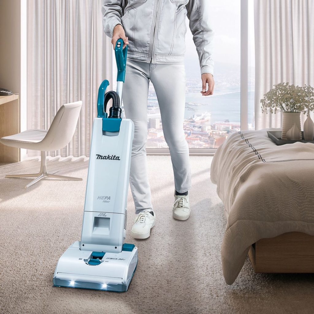 MAKITA Imuri LXT. Kuvassa henkilö imuroimassa hotellihuoneen kokolattiamattoa Imuri LXT:n avulla.