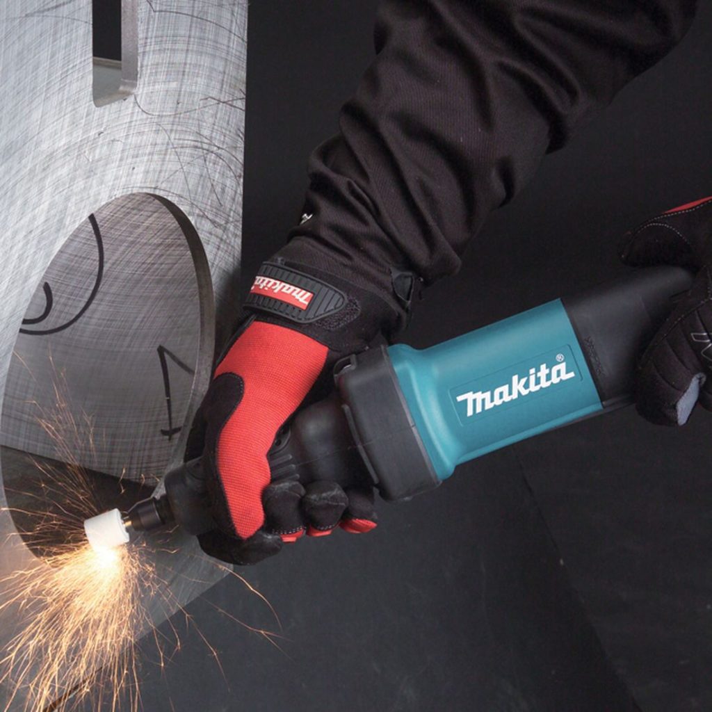 MAKITA Suorahiomakone. Kuvassa henkilö hiomassa teräkseen tehdyn reiän teräviä reunoja Suorahiomakoneen avulla.