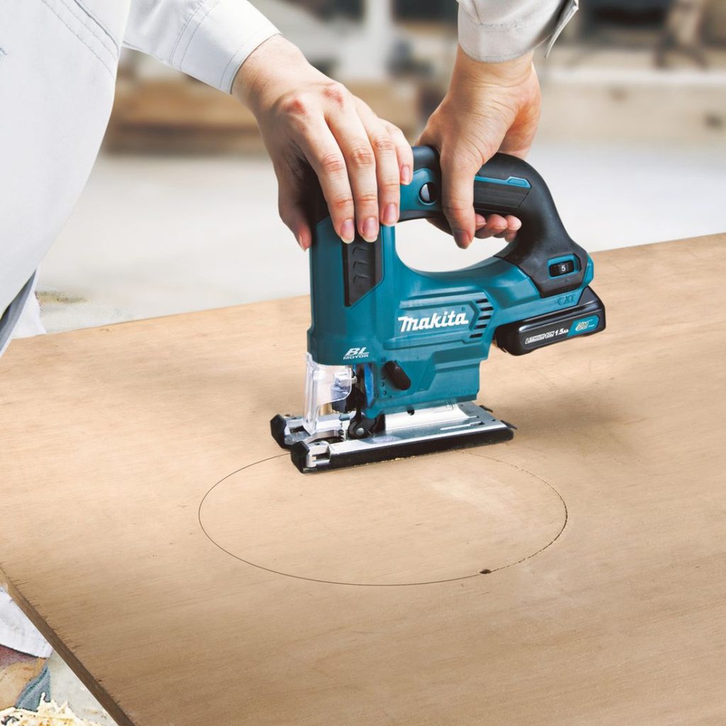MAKITA Pistosaha CXT. Kuvassa henkilö sahaamassa pyöreää reikää vanerilevyyn Pistosaha CXT:n avulla.