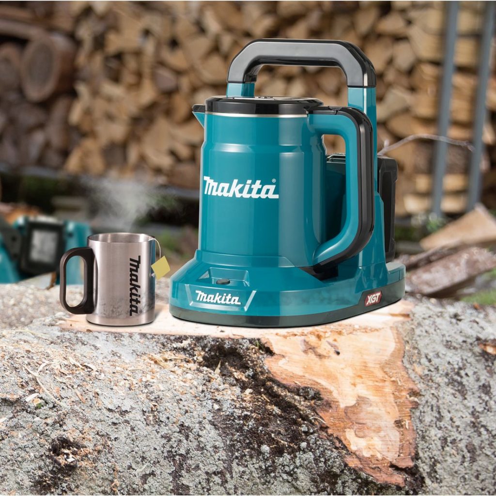 MAKITA Vedenkeitin XGT. Kuvassa Vedenkeitin XGT ja teräksinen muki kaadetun puun päällä.