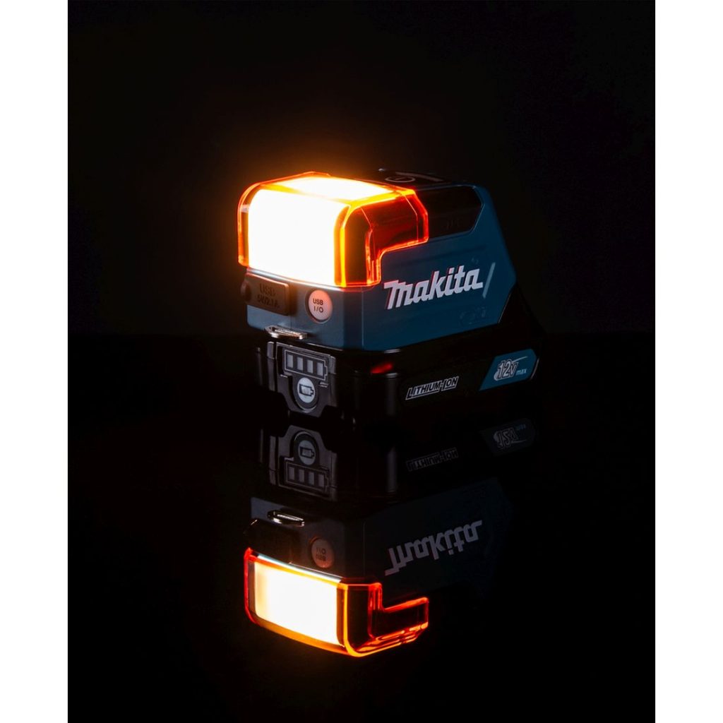 MAKITA LED-valaisin CXT. Kuvassa LED-valaisin CXT pimeässä oikealta etuviistosta valo päällä ja häikäisysuoja kiinnitettynä.