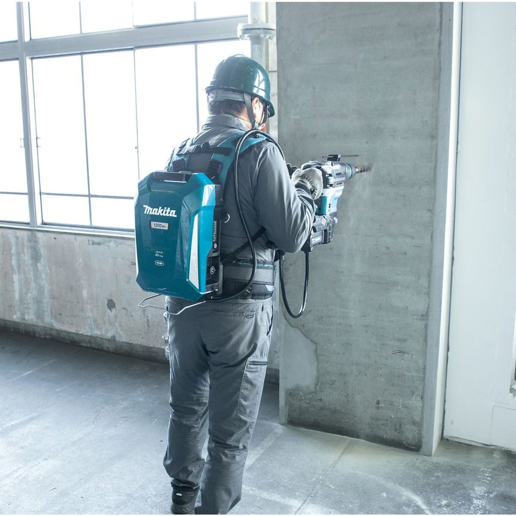 MAKITA Kannettava reppuakku LXT XGT. Kuvassa henkilö poraamassa reikää betoniseinään Kannettava reppuakku LXT XGT akkuporavasaraan yhdistettynä.