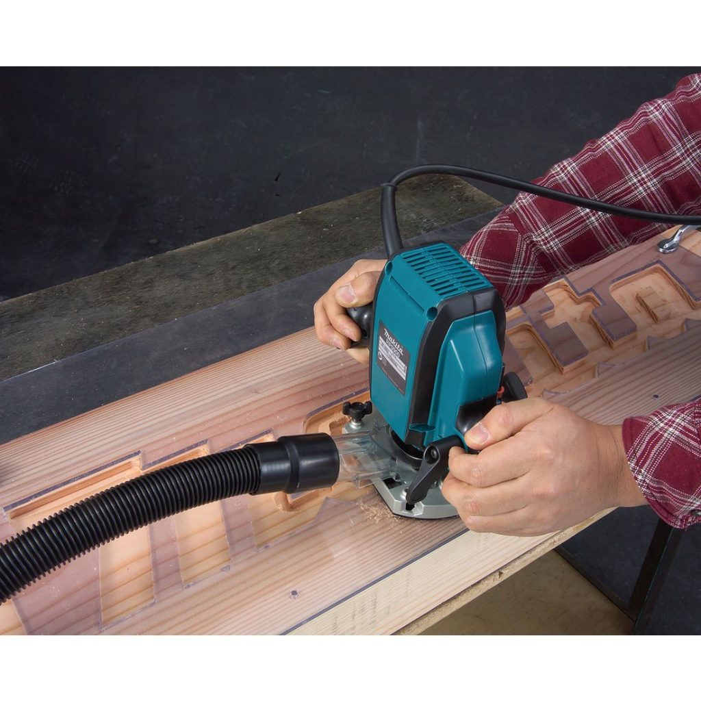 MAKITA Yläjyrsin. Kuvassa henkilö jyrsimässä puuhun Makitan logotekstiä yläjyrsimen avulla akryylisapluunaa hyväksikäyttäen.