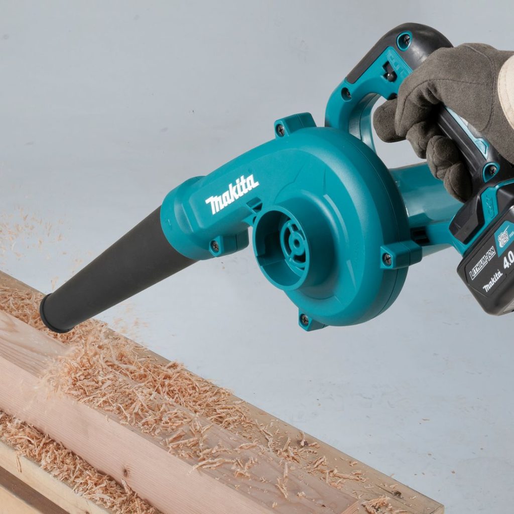 MAKITA Puhallin CXT. Kuvassa henkilö puhaltamassa sanhanpuruja työstetyn puun päältä Puhallin CXT:n avulla.