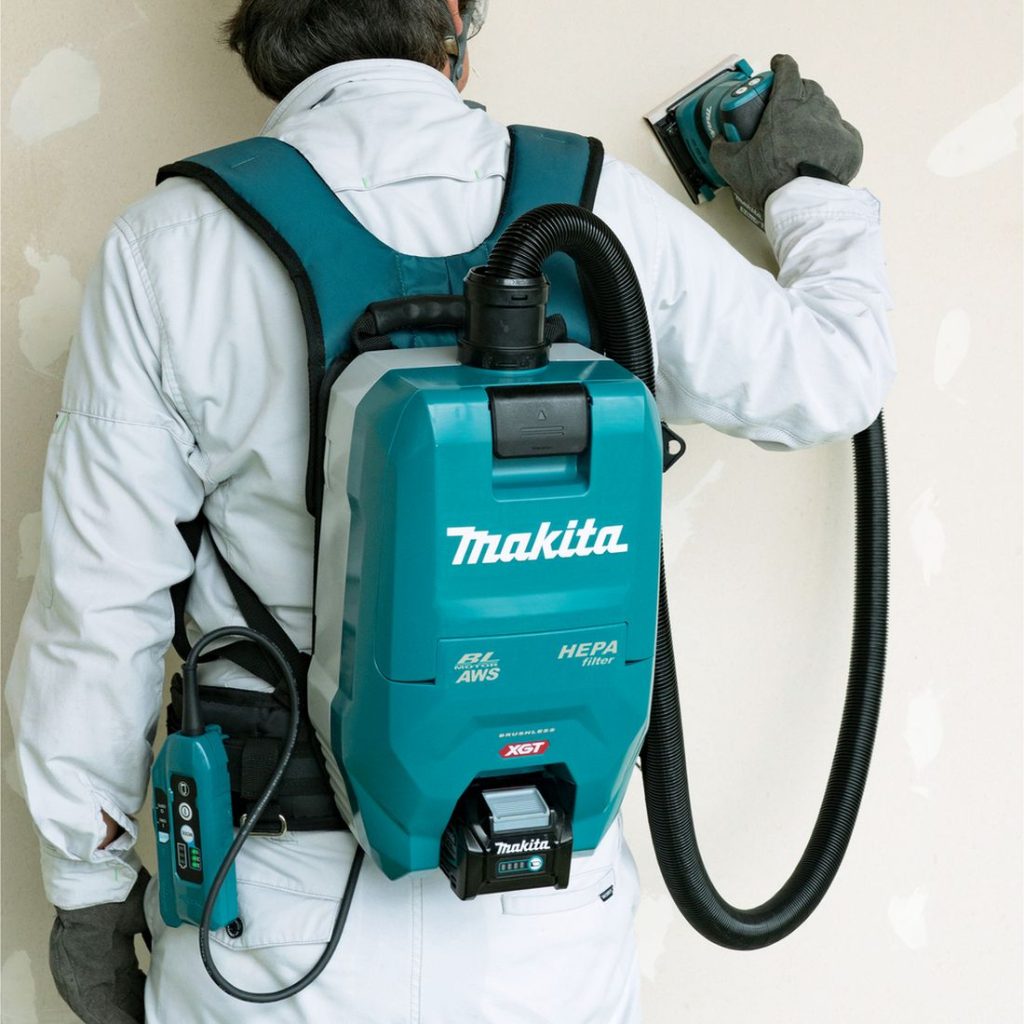 MAKITA Reppuimuri XGT. Kuvassa henkilö hiomassa seinää Reppuimuri XGT:n avulla reppuimuri yhdistettynä hiomakoneeseen.