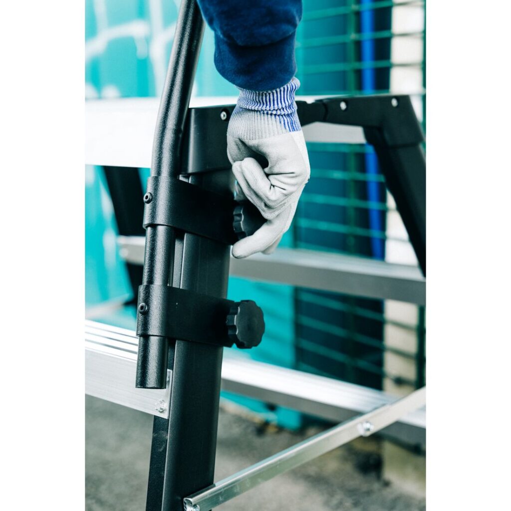 Turvakaide Tikli Grande. Kuvassa henkilö asentamassa turvakaidetta työpukkiin sormimutterin avulla.