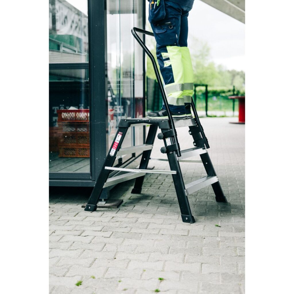 Turvakaide Tikli Grande. Kuvassa henkilö seisomassa työpukin päällä.